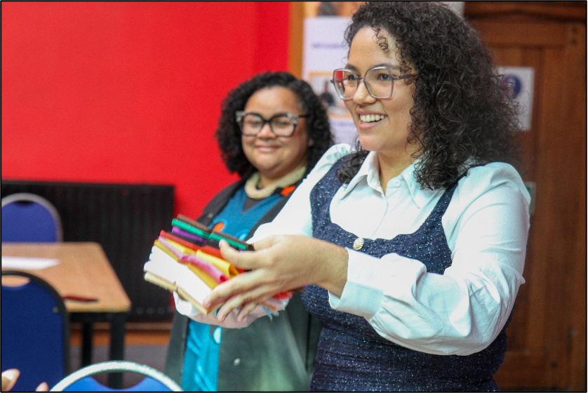Raescla Ribeiro de Oliveira and Professor Iolete Ribeiro da Silva leading a workshop. they are smiling, and holding bundles of fabric.