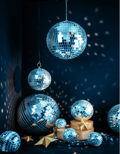 Several mirrored disco balls of different sizes hang and sit on a dark surface, reflecting light around the room. Gold star ornaments are placed among the disco balls, with a deep blue background that enhances the shimmering reflections