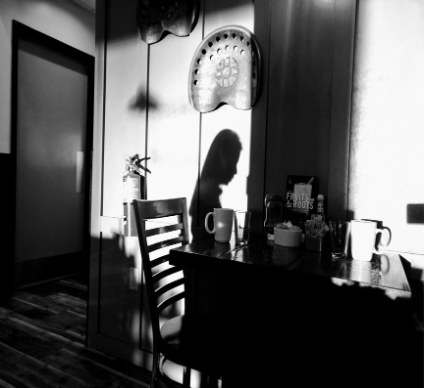 A kitchen with a table laid for tea. No people are present but the shadow of a person is on the wall behind the table.